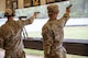Women in U.S. Army uniforms firing pistols on indoor pistol range.