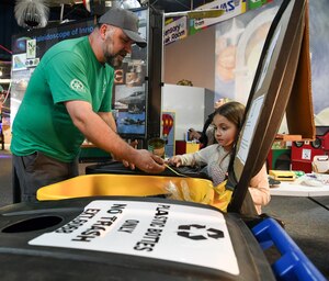 A man, standing at left, shows a little girl, at right, how to tell if a can is made of aluminum by using a magnet during a Global Recycling Day event at the Hands-On Science Center in Tullahoma, Tenn.