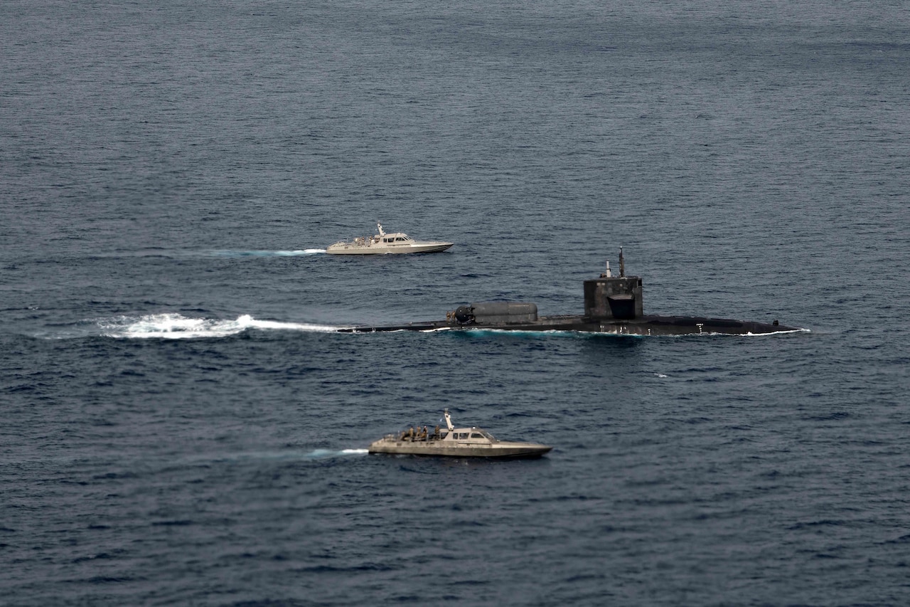 Two patrol boats and submarine sail in formation.