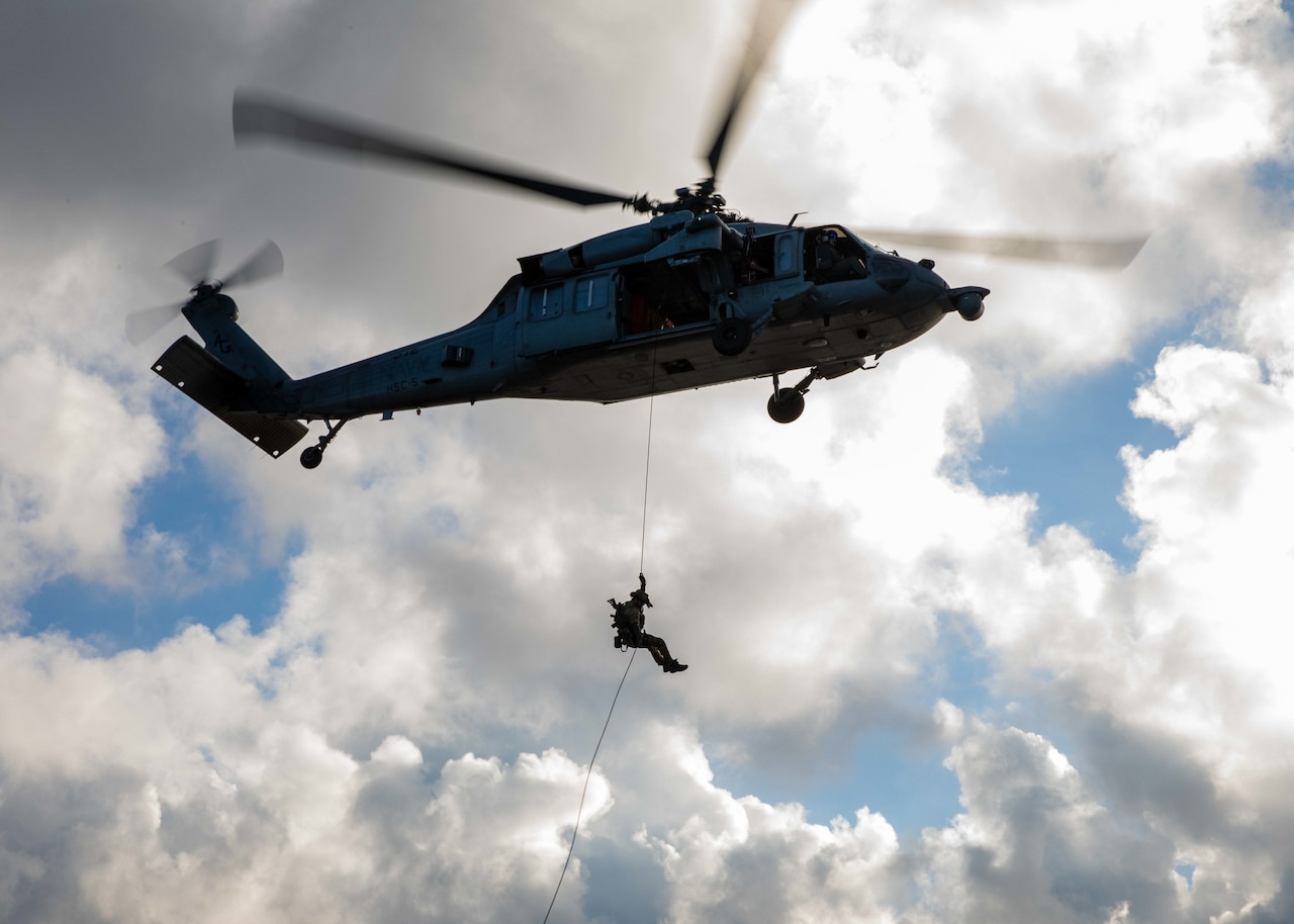 A sailor rappels down a rope attached to a helicopter.
