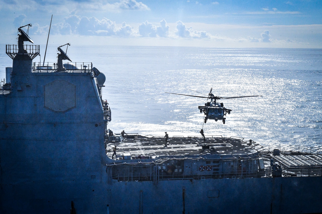 Sailors rappel down a rope attached to a helicopter on to a ship at sea.