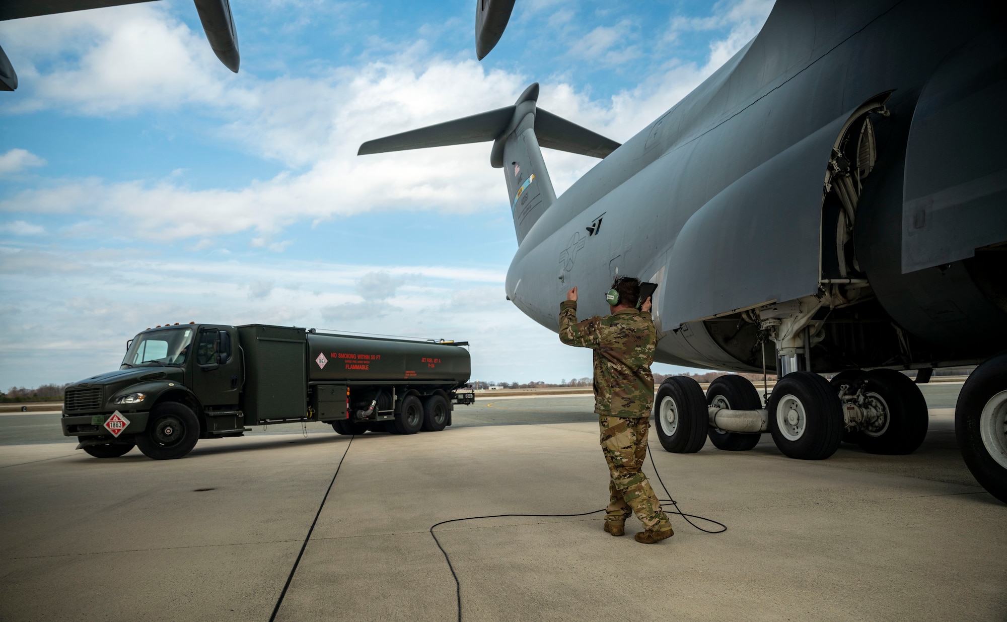 Staff Sgt. Kyle Hewitt, 9th Airlift Squadron flight engineer, marshals an R-11 Refueler next to a C-5M Super Galaxy during a wet wing defuel at Dover Air Force Base, Delaware, March 1, 2023. Aircrew with the 9th AS test out new capabilities that allow the C-5 to act as a mobile fuel station and deposit fuel from the aircraft fuel tanks, into tankers standing by. (U.S. Air Force photo by Staff Sgt. Marco A. Gomez)