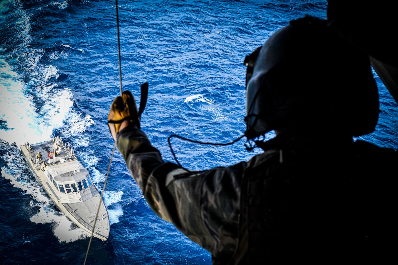 A Navy SEAL looks out of an airborne helicopter as a ships sails below.