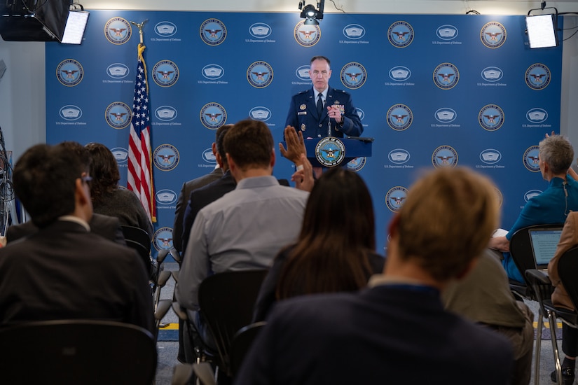 A uniformed service member stands behind a lectern in front of a group.