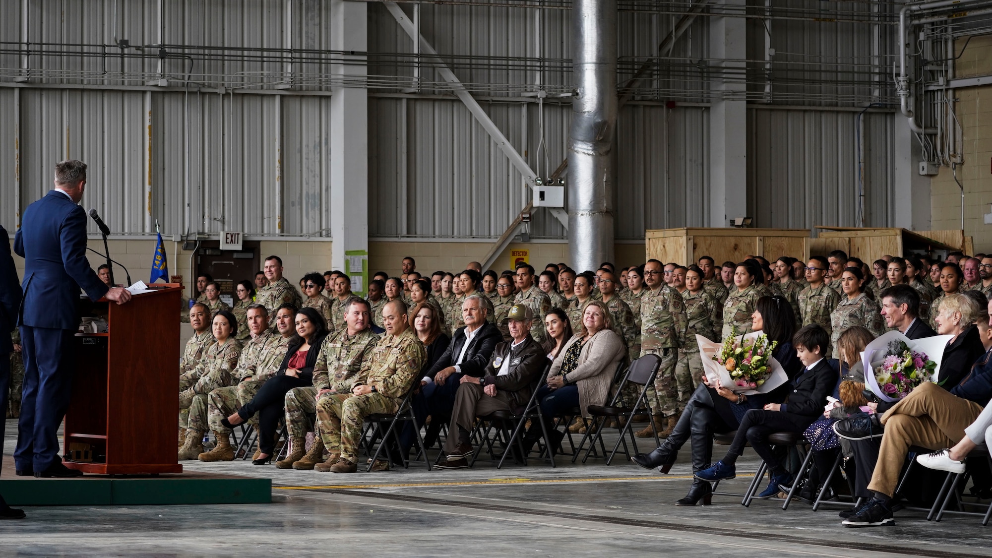 A man gives a speech to a large crown of seated people.