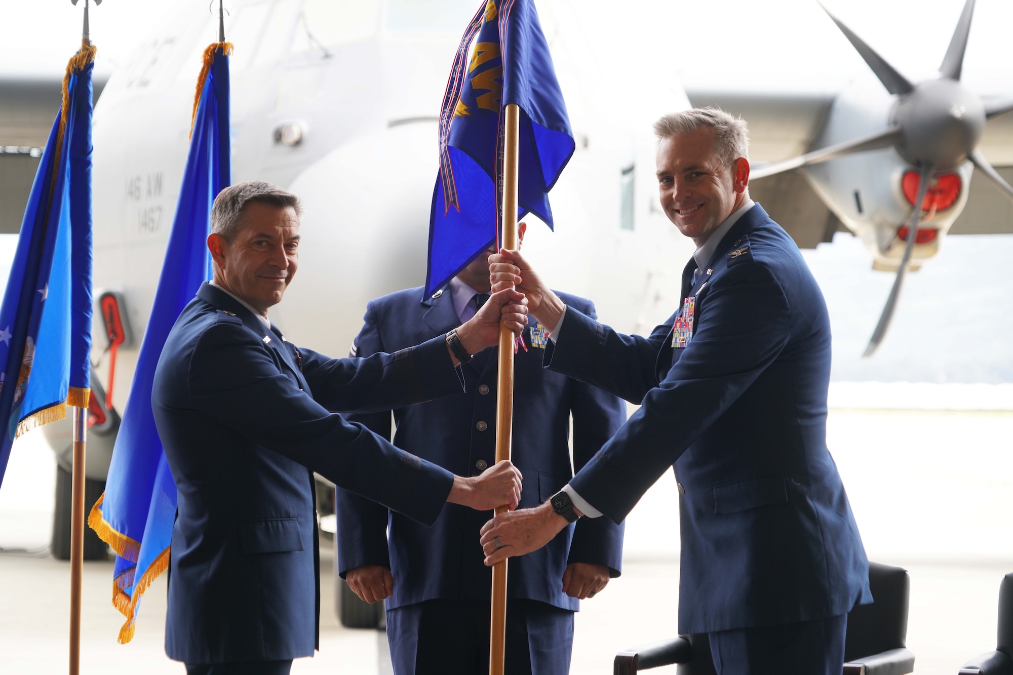 Two men hold a unit flag and smile at the camera.
