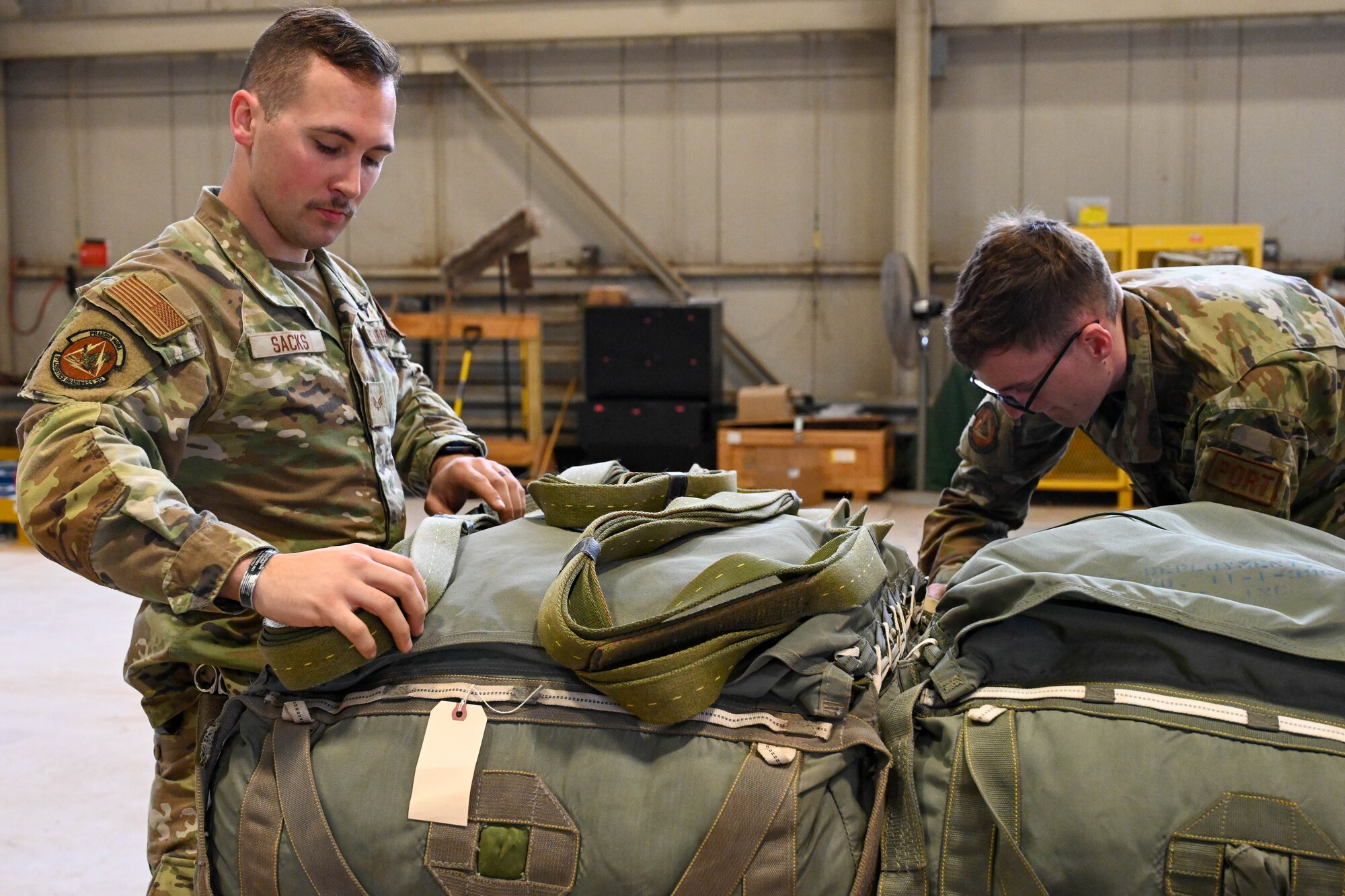 U.S. Air Force Senior Airman Logan Sacks, 97th Logistics Readiness Squadron (LRS) unilateral aircrew training (UAT) rigging supervisor, and Senior Airman Jack Woodmansey, 97 LRS UAT rigging element member, load a duel row airdrop system in preparation for a large force exercise at Altus Air Force Base, Oklahoma, March 23, 2023. The flight assembled eight pallets for air-drop training during the severe weather exercise. (U.S. Air Force photo by Senior Airman Trenton Jancze)
