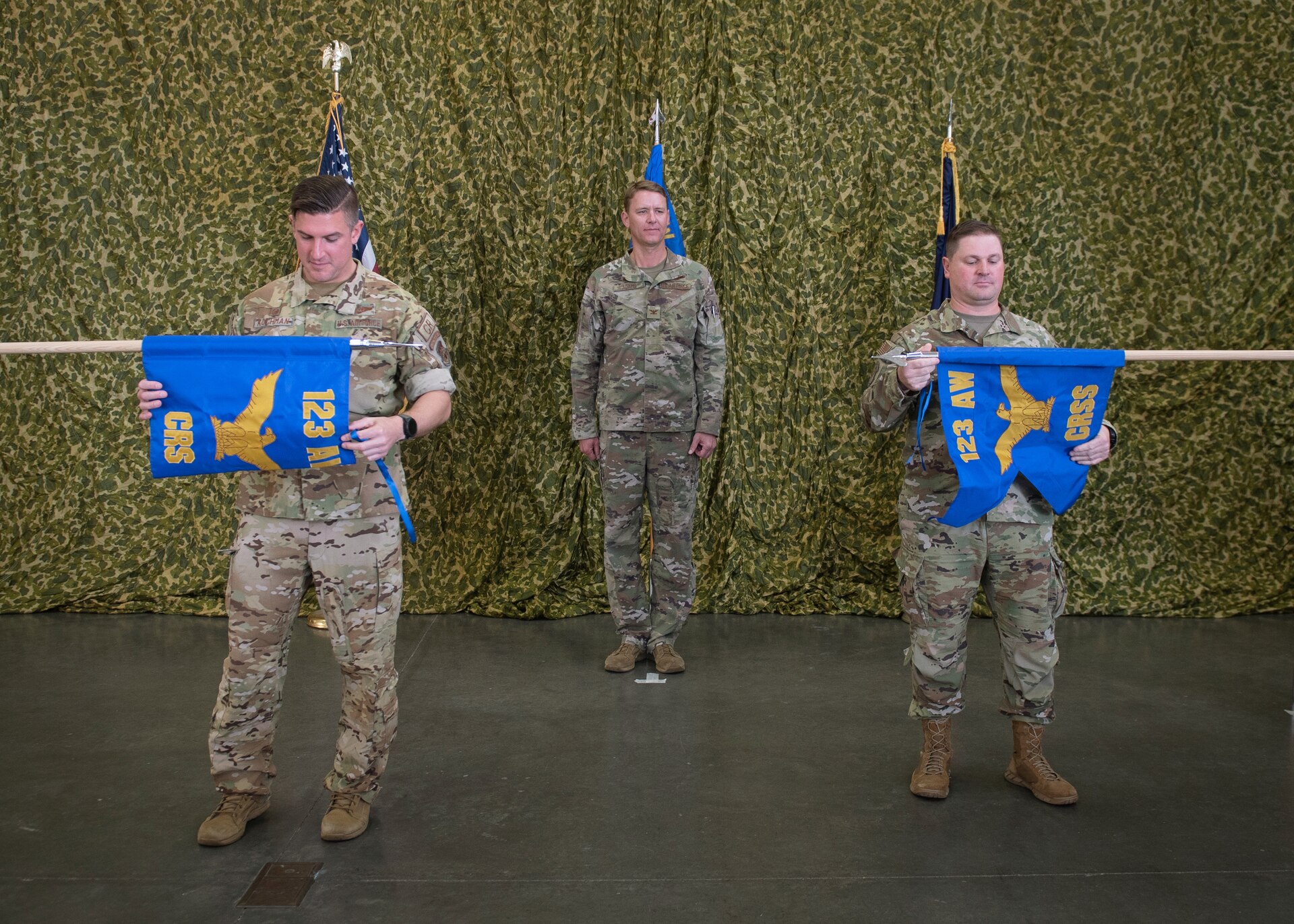 Maj. Andrew Kochman, left, commander of the 123rd Contingency Response Squadron, and Lt. Col. Kevin Krauss, right, commander of the 123rd Contingency Response Support Squadron, unfurl new squadron guidons Oct. 15, 2022, during a ceremony at the Kentucky Air National Guard Base in Louisville, Ky., as Col. Ryan Adams, commander of the 123rd Contingency Response Group looks on. The units received new names to better reflect their mission sets. (U.S. Air Force photo by Staff Sgt. Clayton Wear)