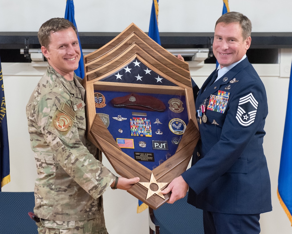 Chief Master Sgt. Karl Grugel, right, senior enlisted leader of the 123rd Special Tactics Squadron, is presented with a shadow box during his retirement ceremony at the Kentucky Air National Guard Base in Louisville, Ky., Dec. 10, 2022. Grugel served the Air Force and Air National Guard for 31 years. (U.S. Air National Guard photo by Staff Sgt. Clayton Wear)