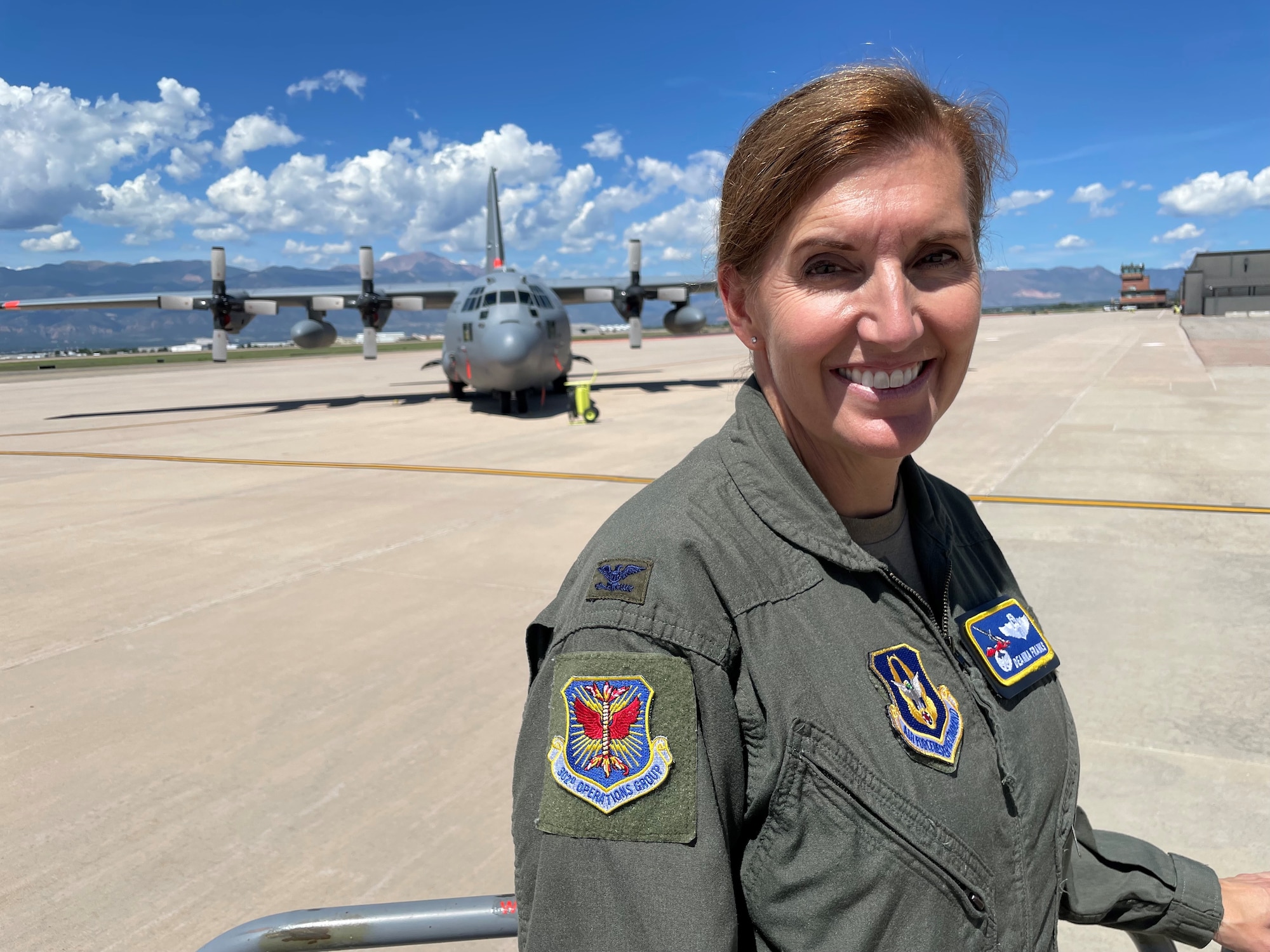 Female in military flying uniform stands in front of military plane on flightline