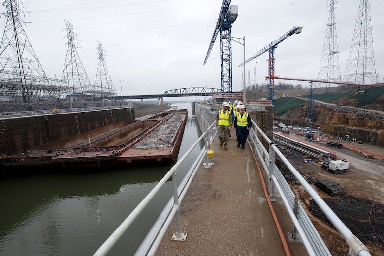 Lt. Col. Joseph Sahl, U.S. Army Corps of Engineers Nashville District commander, leads a group of stakeholders on a tour of Kentucky Lock and the Kentucky Lock Addition Project March 22, 2023, on the Tennessee River in Grand Rivers, Kentucky. He is having a conversation with Cmdr. Jennifer Andrew, commander of U.S. Coast Guard Marine Safety Unit Paducah, as the group walked on the coffer dam and future downstream approach wall during the tour. A vessel and barges approach the downstream active lock on the left of the photo and construction of the new lock chamber can be seen on the right of the photo. (USACE Photo by Lee Roberts)