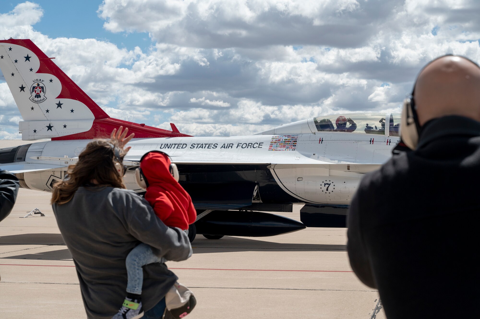 Photo of a mother and child waving at the people inside of an aircraft passing by.