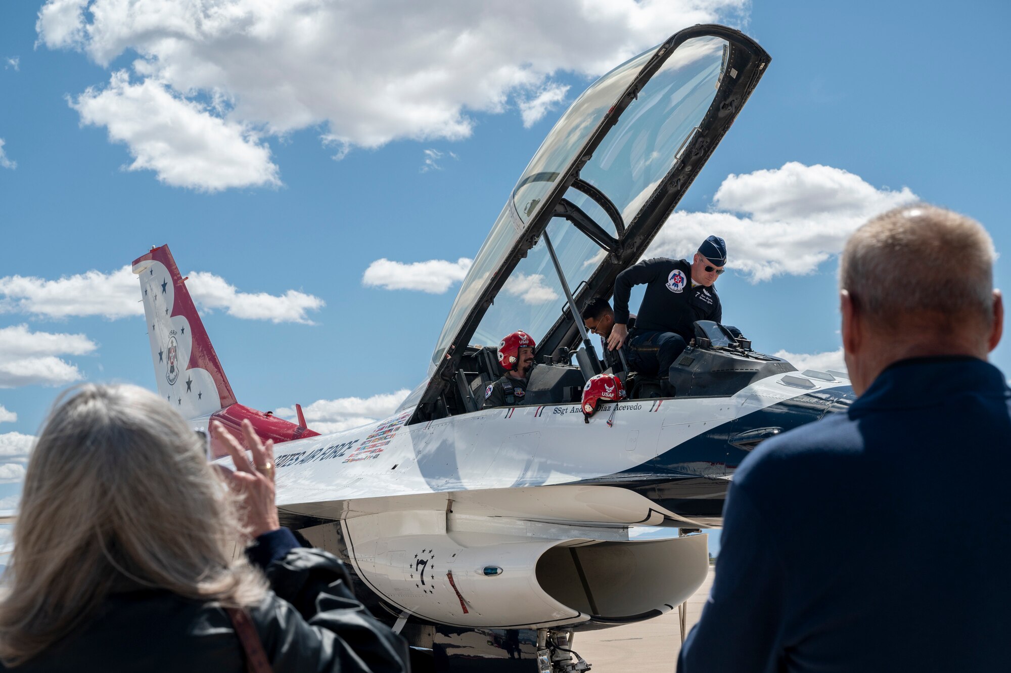 Photo of two people boarding a two-seater fighter jet with two people watching in the foreground.