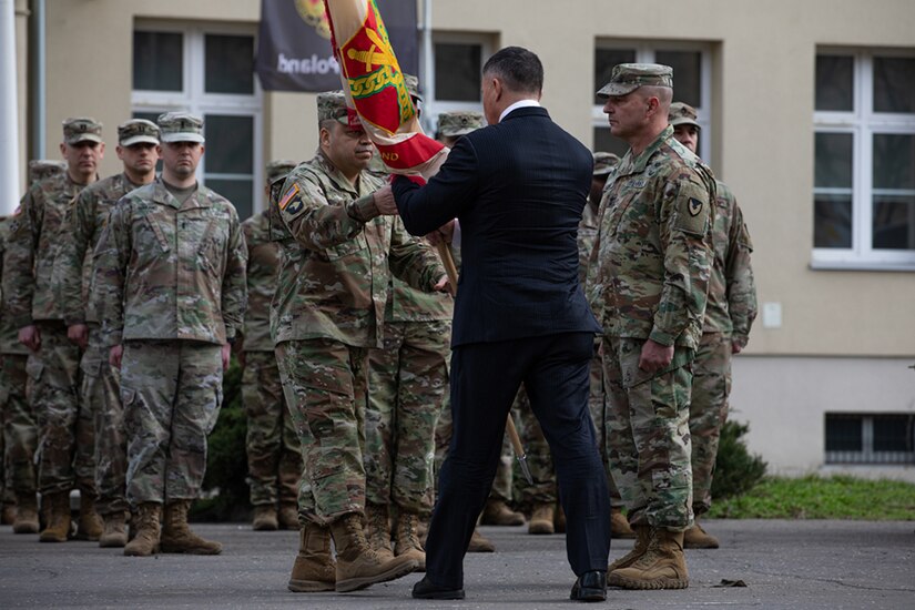 Two people exchange a flag as others look on.