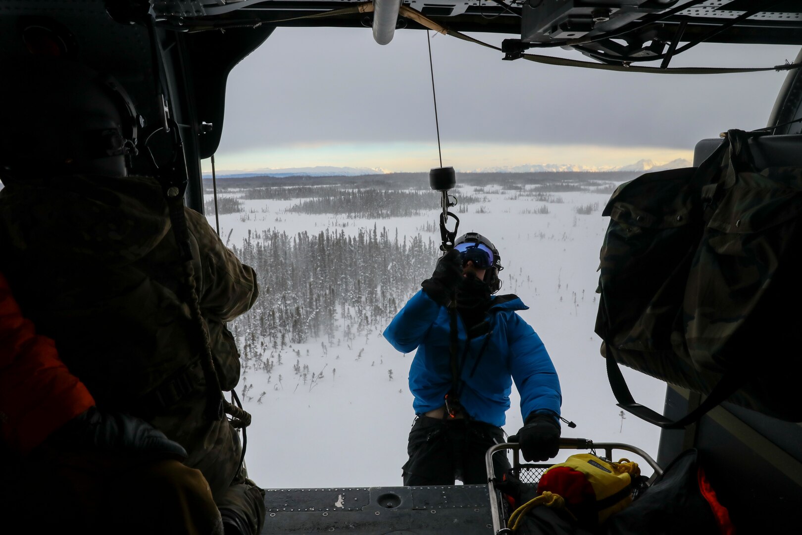 Alaska Air National Guard Staff Sgt. Kaden Wernofski, a 210th Rescue Squadron special missions aviator, operates the hoist to lift a 212th RQS pararescueman into an HH-60G Pave Hawk helicopter during a training mission over the Lower Susitna Valley near Anchorage, Alaska, Feb. 7, 2023. The HH-60G and rescue personnel along with a 211th RQS HC-130J Combat King II aircraft sit alert for the federal search and rescue mission across Alaska’s vast Arctic region.