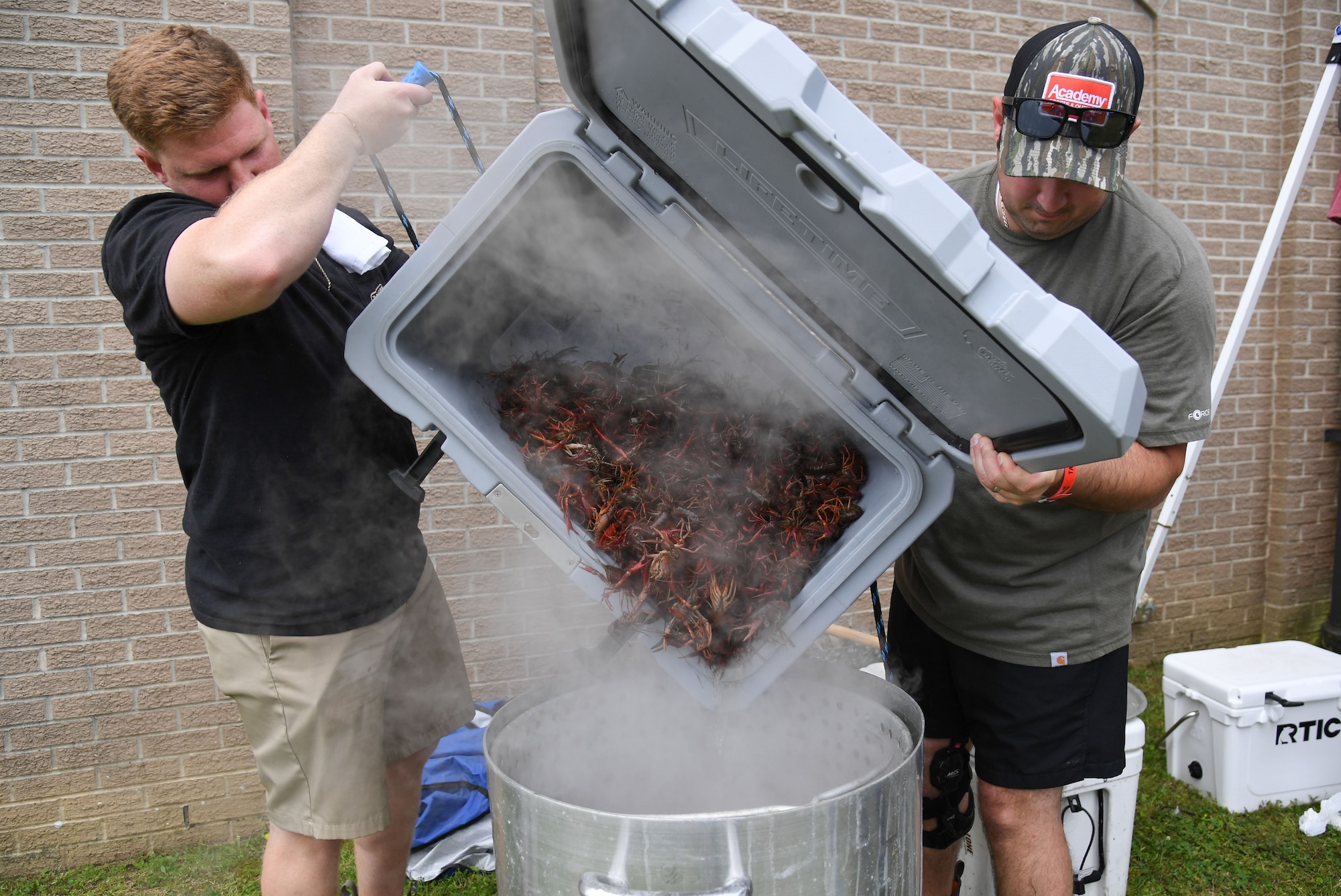 U.S. Air Force Staff Sgt. Anthony Ryan, 81st Security Forces Squadron armory NCO in charge, and Tech. Sgt. Tino Mong, 81st SFS unit deployment manager, Marsh Ops team members, pour live crawfish into a pot of boiling water during the 11th Annual Crawfish Cook-Off outside the Bay Breeze Event Center at Keesler Air Force Base, Mississippi, March 24, 2023.