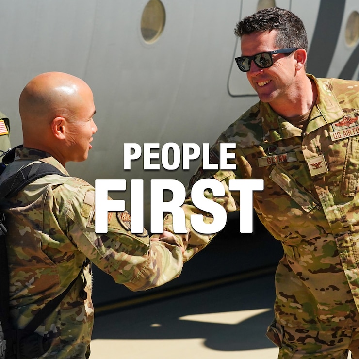 A white graphic text displaying the words People First in front of a photograph of two California Air National Guard military members shaking hands in front of a military C-130J aircraft.
