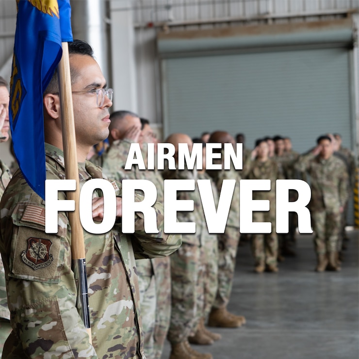 A white graphic text displaying the words Airmen Forever in front of a photograph of an Airman holding his squadron's guideon while standing in formation inside a hangar.