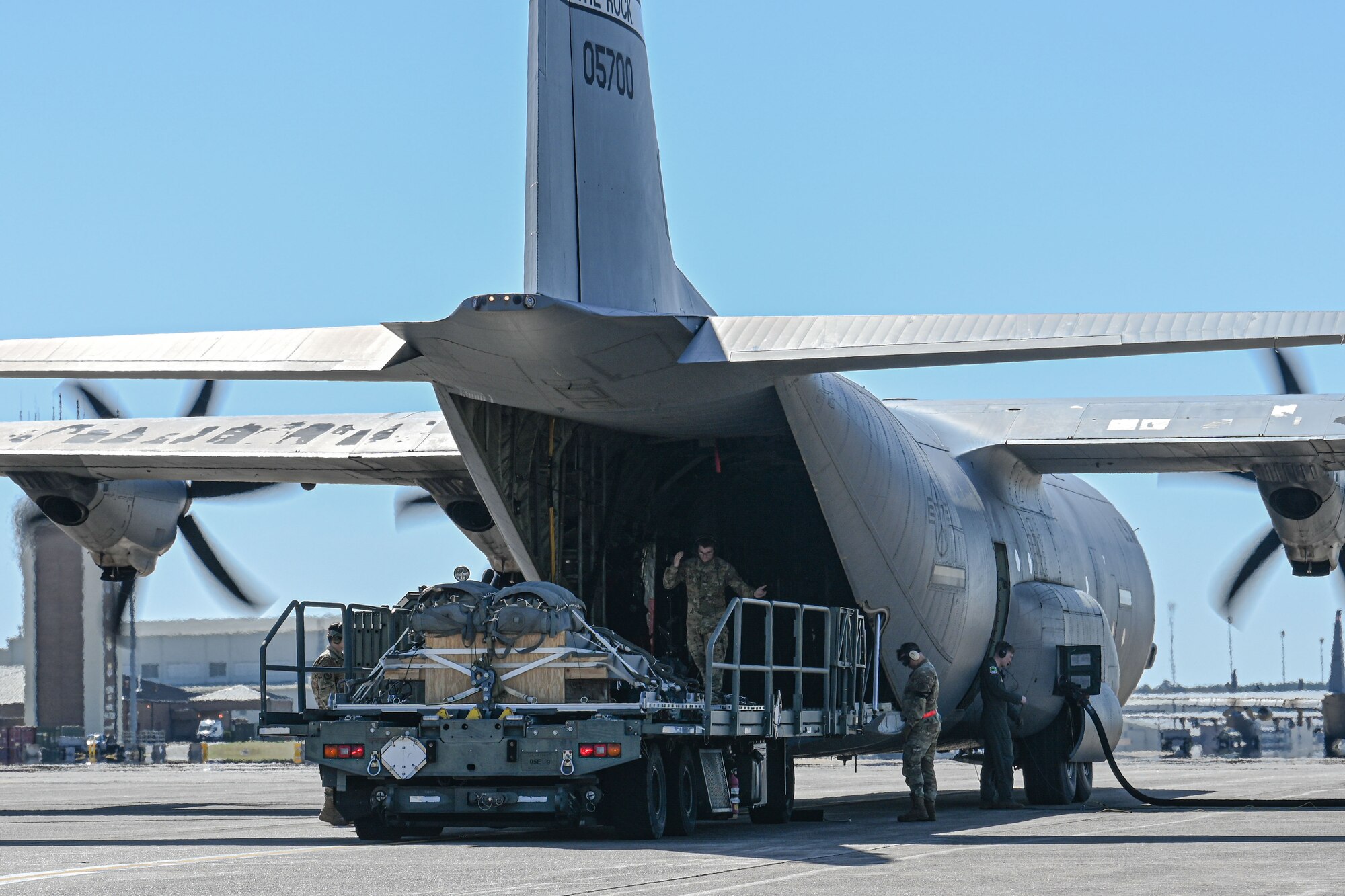 A C-130 is refueled and loaded with cargo on the flightline, while the engines run.