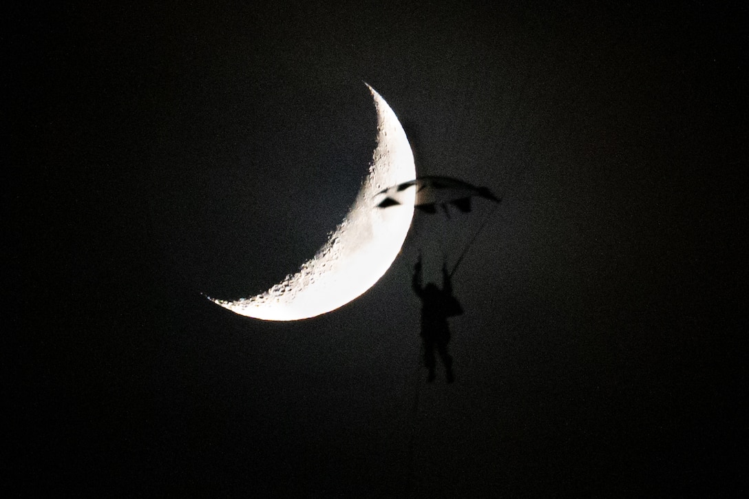 A soldier parachutes at night with a crescent moon in the background.