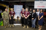 A group of six men and two women stand in front of a banner that states "Your Journey Starts Here."