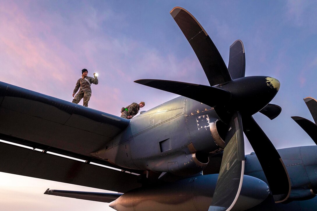 Airmen stand on the wing of a military aircraft to perform an inspection.