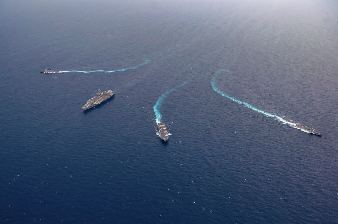 Four ships sail in formation in a body of water as seen from above.