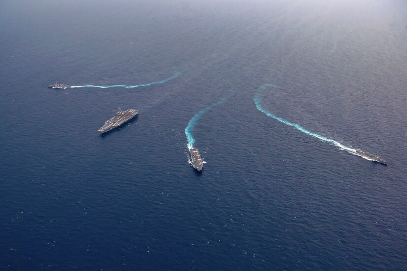 Four ships sail in formation in a body of water as seen from above.