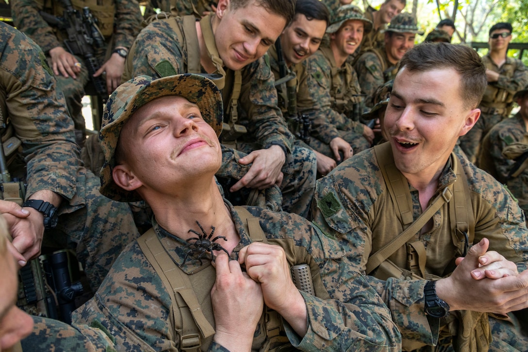 A Marine  smiles as a large spider walks along his neck.