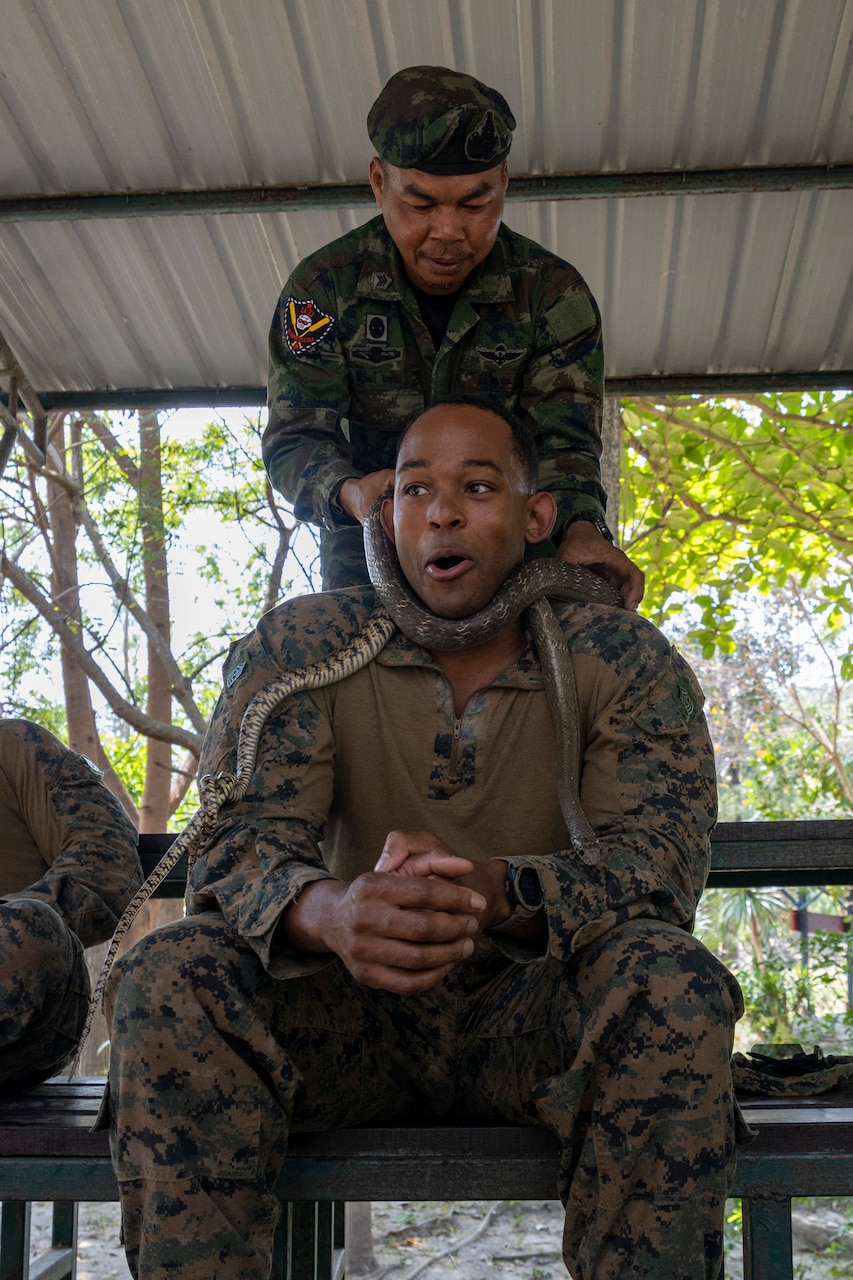 A Marine smiles as another Marine places a snake around his neck.