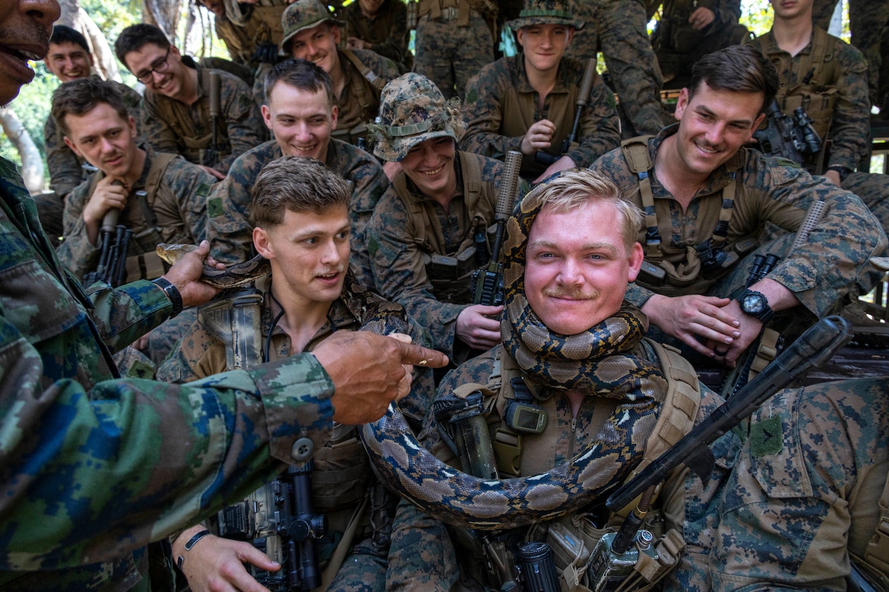 A Marine smiles as a snake is wrapped around his neck while other Marines look on.