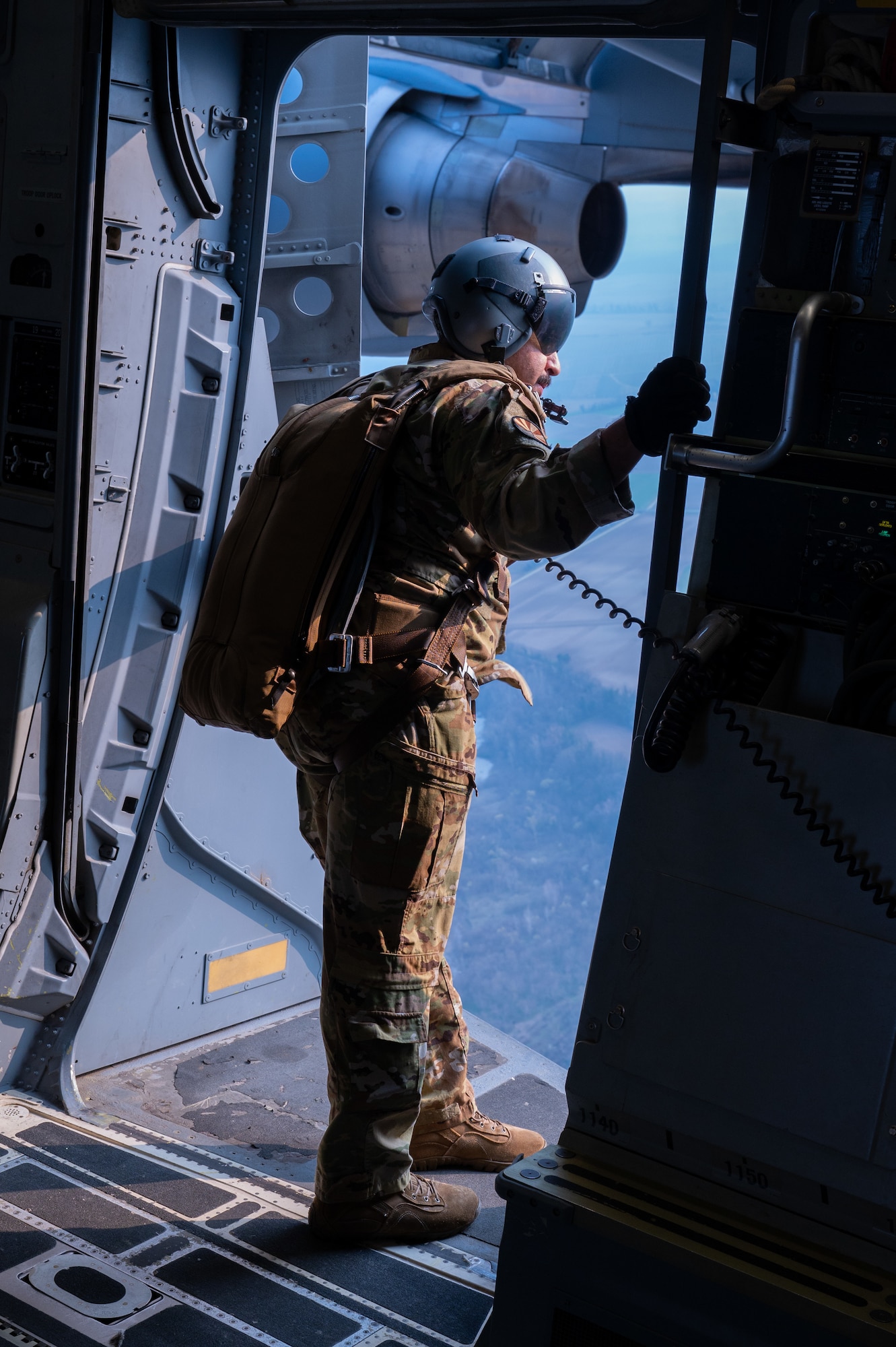 A loadmaster stands in the open door frame of a C17 Globmaster as it flies across Italy.