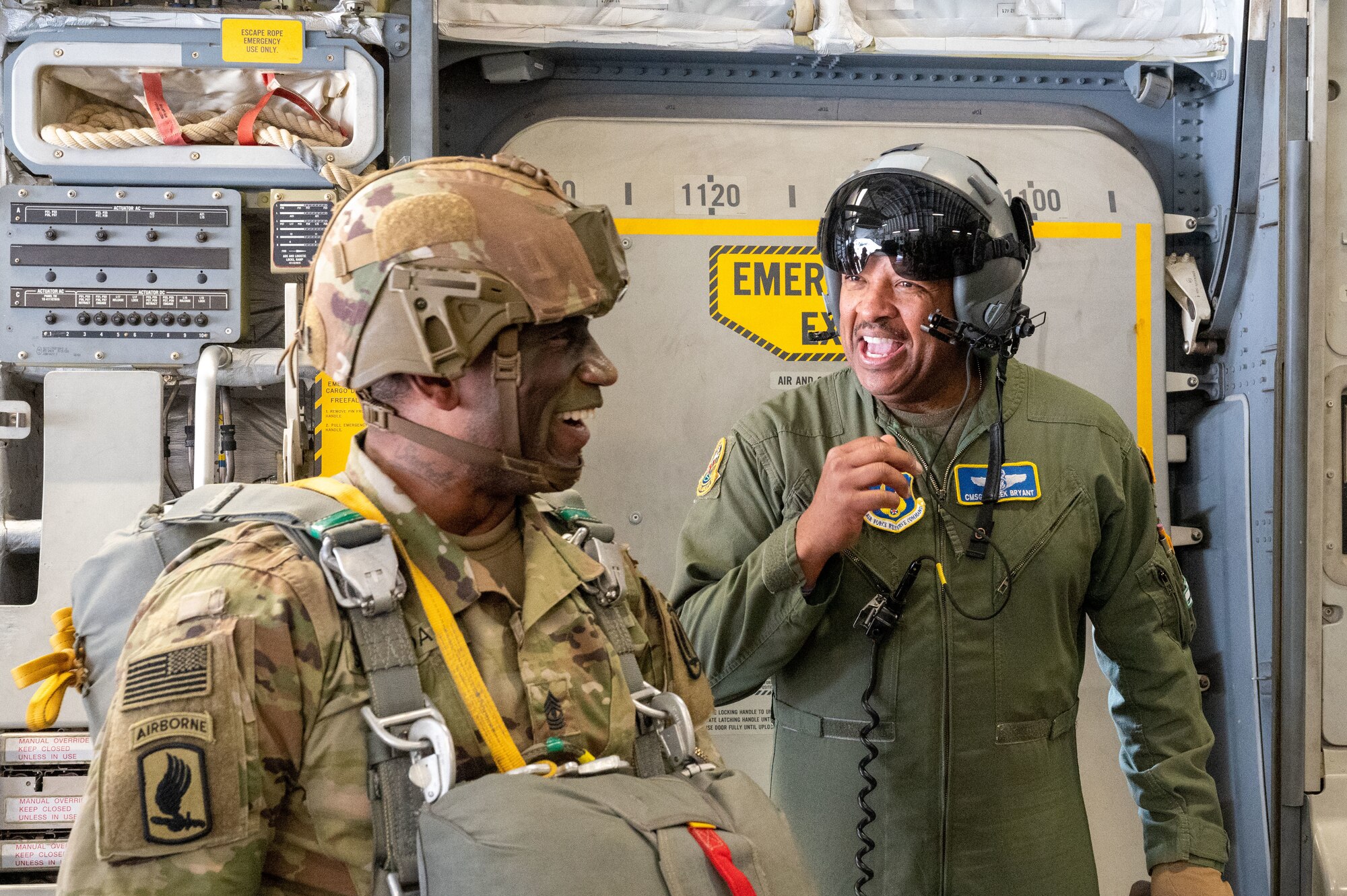 U.S. Air Force Chief Derek Bryant wears a flight suit and helmet as he talks to a 1st Sgt. of the U.S. Army who is wearing his parachute gear and face paint at the crew door of a C17.