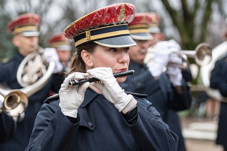 An Army musician plays the flute; other musicians play in the background.