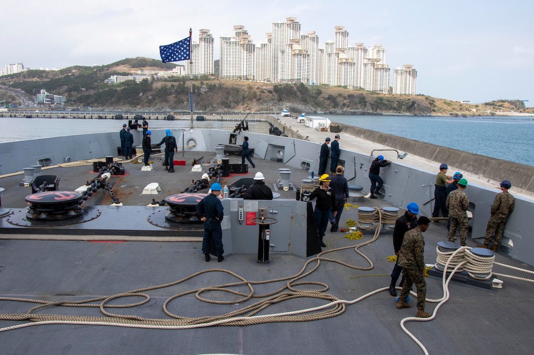 Sailors and Marines stand on the deck of a ship with ropes lying around them.