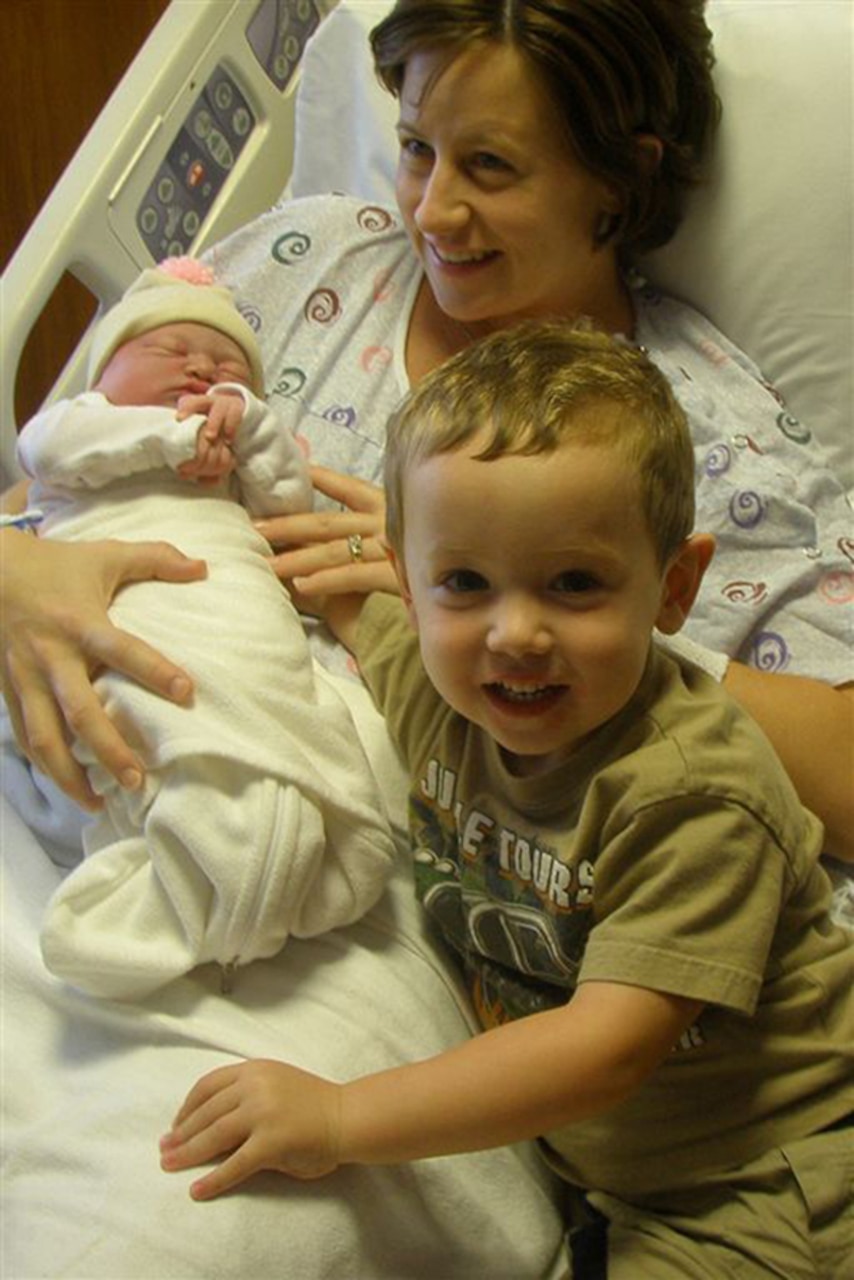 A mother holds her newborn with her little boy at her bedside.