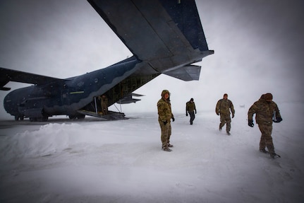 Members of the 32-person delegation of soldiers, airmen and civilians from the Alaska National Guard and Department of Military and Veterans Affairs exit an Alaska Air National Guard HC-130J Combat King II aircraft in Gambell, Alaska, under stormy conditions March 28, 2023. The delegation travelled to Gambell for a ceremony honoring 16 Alaska Army National Guard First Scouts for their heroism.