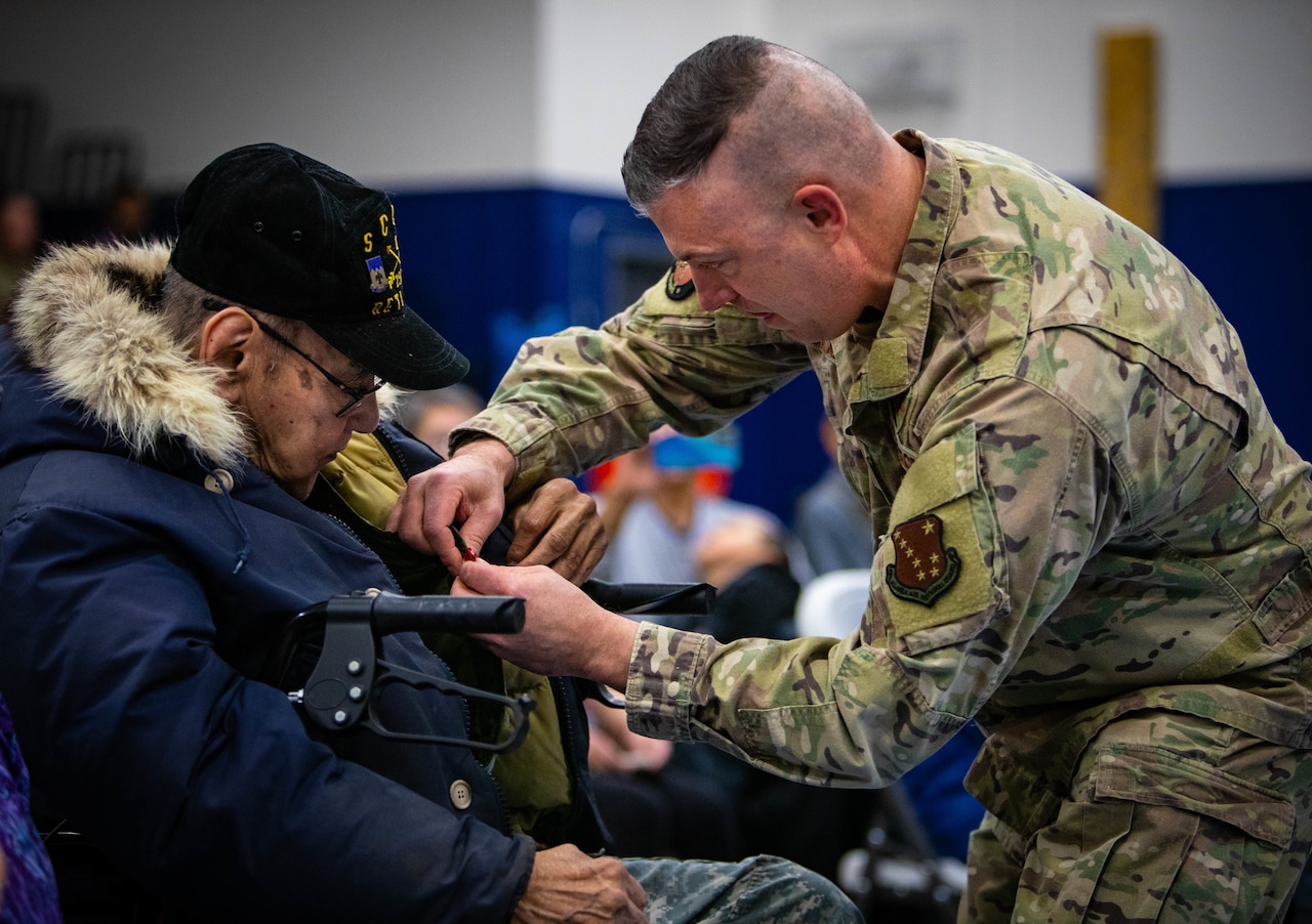 A soldier pins a medal to a man’s jacket.