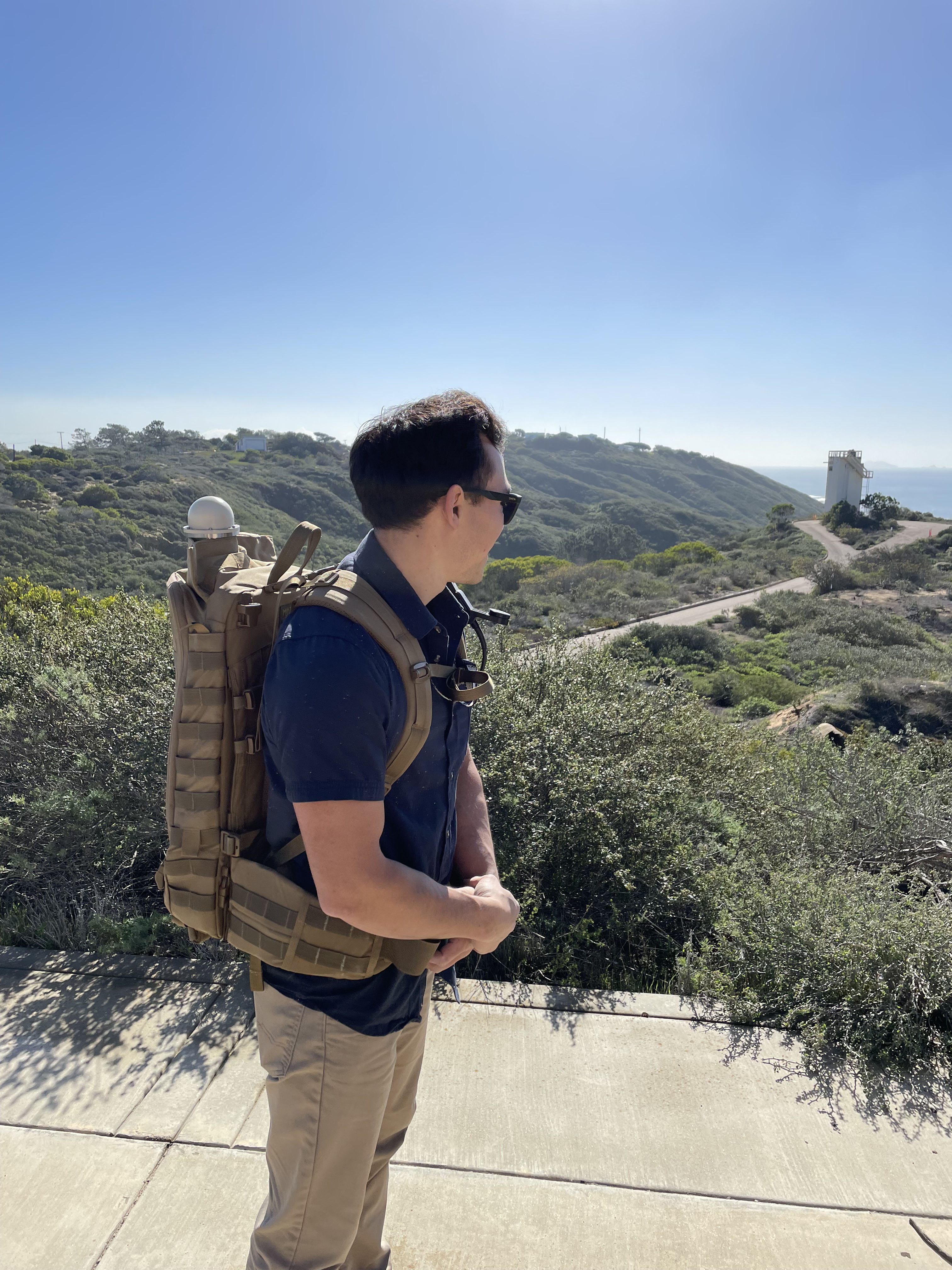 a person poses outside wearing a backpack with a silver orb sitting on top