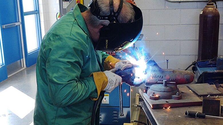 A man in safety gear stands up to weld a gear puller.