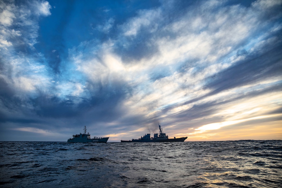 Two ships sit side by side in the ocean at twilight.