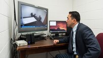 Army CID agent watches special agents question a suspect on closed circuit television