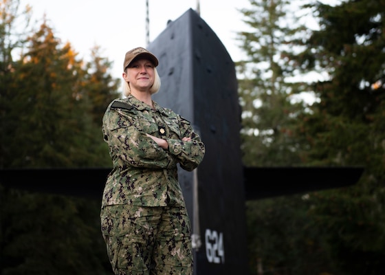 Smiling woman in uniform posing with crossed arm on submarine with topside behind her