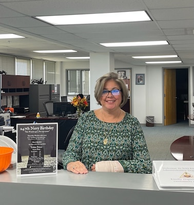 Smiling woman with glasses in green civilian attire sitting at desk