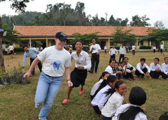 Joy Chase running around with children sitting on grass with a student running after her