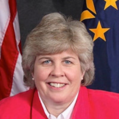 Smiling woman in civilian attire posing for official photo with flags in the background