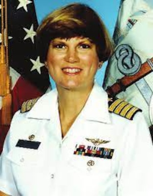 Smiling woman in white uniform posing for official photo with USA flag in the background