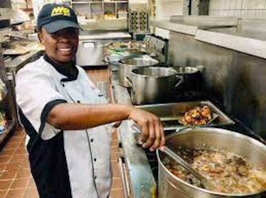 Smiling woman in chef uniform stirring the pot and posing for the camera