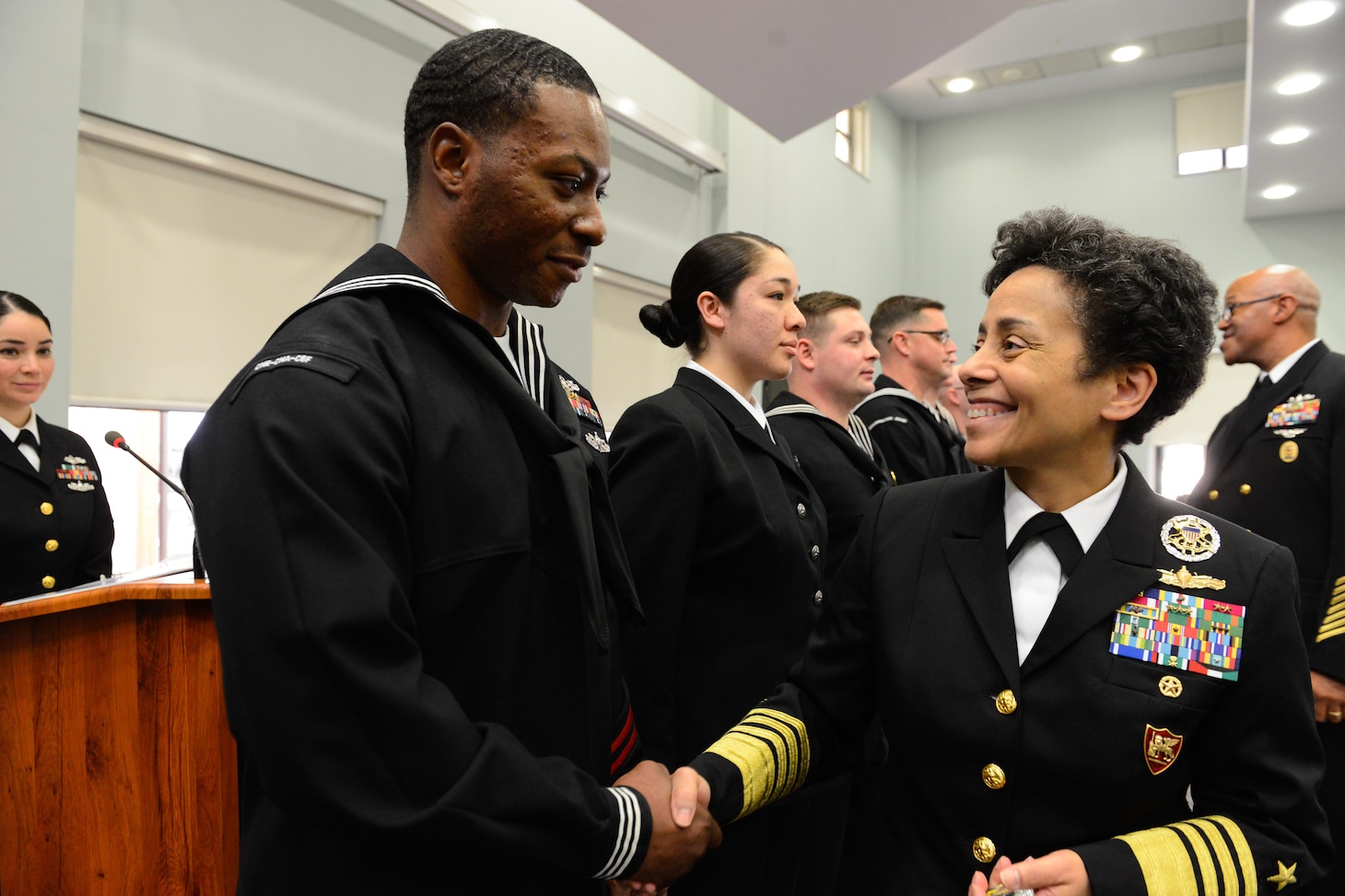 Michelle Howard on the right in uniform smiling and shaking with Sailor standing