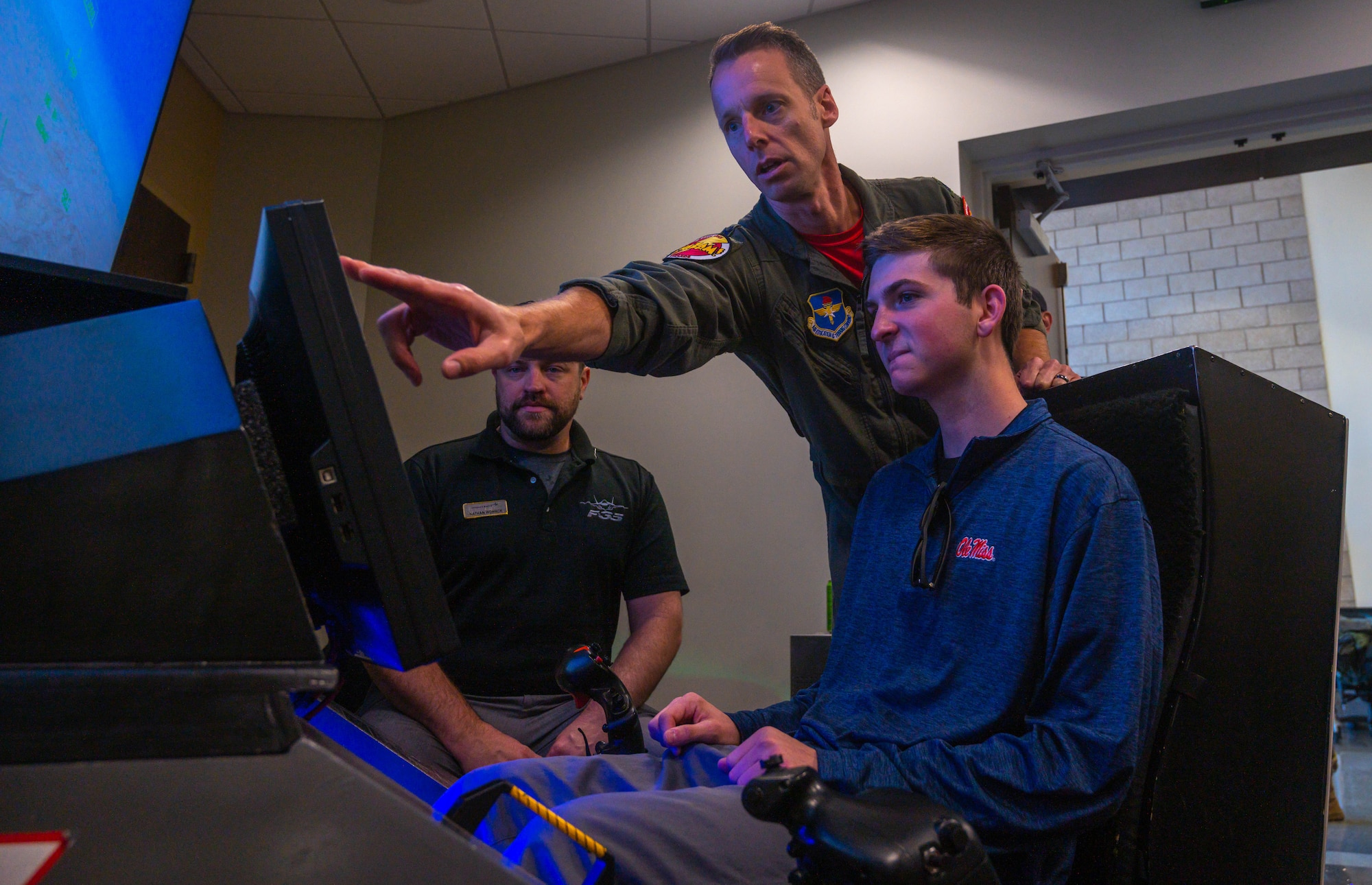 U.S. Air Force Lt. Col. Joshua Larsen, 56th Operations Support Squadron commander, guides a family member of an honorary commander on how to operate a flight simulator during an HCC Rodeo March, 24, 2023, at Luke Air Force Base, Arizona.